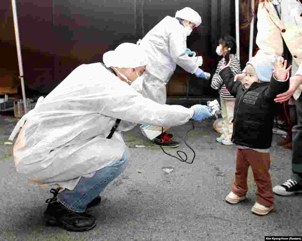 Cadre medicale în costume de protecție verifică nivelul de radiații al copiilor veniți din zona de evacuare, în apropierea centralei nucleare Fukushima Daini din Koriyama, Japonia, 13 martie 2011.