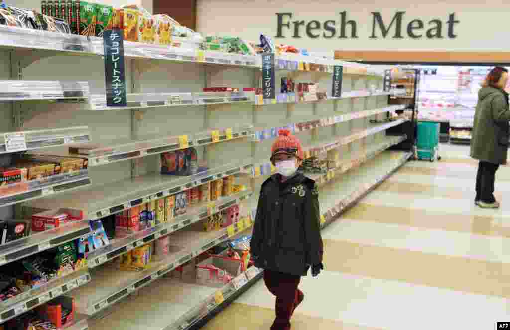 Un băiat cu mască pe față trece pe lângă rafturile aproape goale ale unui supermarket din orașul Akita aflat în nord-vestul țării, pe 15 martie 2011. Psihoza cumpărăturilor cuprinsese întreaga țară după cutremurul și tsunamiul din 11 martie din estul Japoniei, precum și după criza nucleară declanșată în prefectura Fukushima. Criza nucleară a Japoniei a atins momente critice pe 15 martie, când două explozii au zguduit reactoarele atomice afectate de cutremur, producând incendii de mari proporții și emisii de radiații cu mult peste normal.